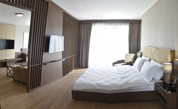 Habitación de hotel con una cama grande, un escritorio, una silla, un televisor y una ventana con cortinas.