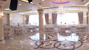 A spacious banquet hall with multiple round tables and chairs, marble flooring, and classical architectural columns.