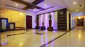 En moderne hotellobby med et marmorgulv, en receptionsdisk og tre store plantekasser.