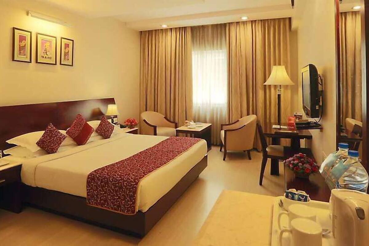 A hotel room with a large bed, two bedside tables, a desk with a chair, a mirror, and a window with curtains.