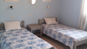 A room with two single beds, a small bedside table, a wall-mounted mirror, and two wall art pieces. - Almiros Apartments (Corfu)