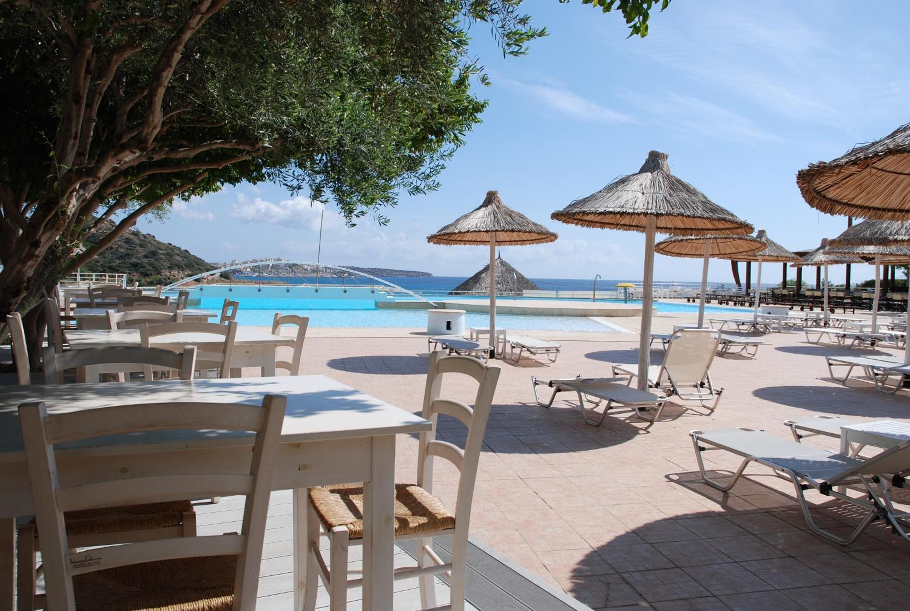 A poolside area with lounge chairs, tables, and umbrellas, overlooking a clear blue pool and a distant view of a coastal landscape.