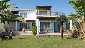 A two-story house with a balcony, a patio with outdoor furniture, and tropical plants. - Almiros Apartments (Corfu)
