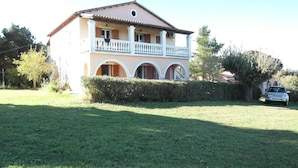 A two-story house with a balcony, a lawn, and a parked car. - Almiros Apartments (Corfu)