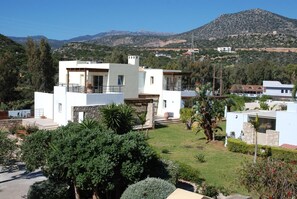 A modern two-story house with a flat roof, surrounded by lush greenery and a mountainous backdrop. - Almiros Apartments (Corfu)