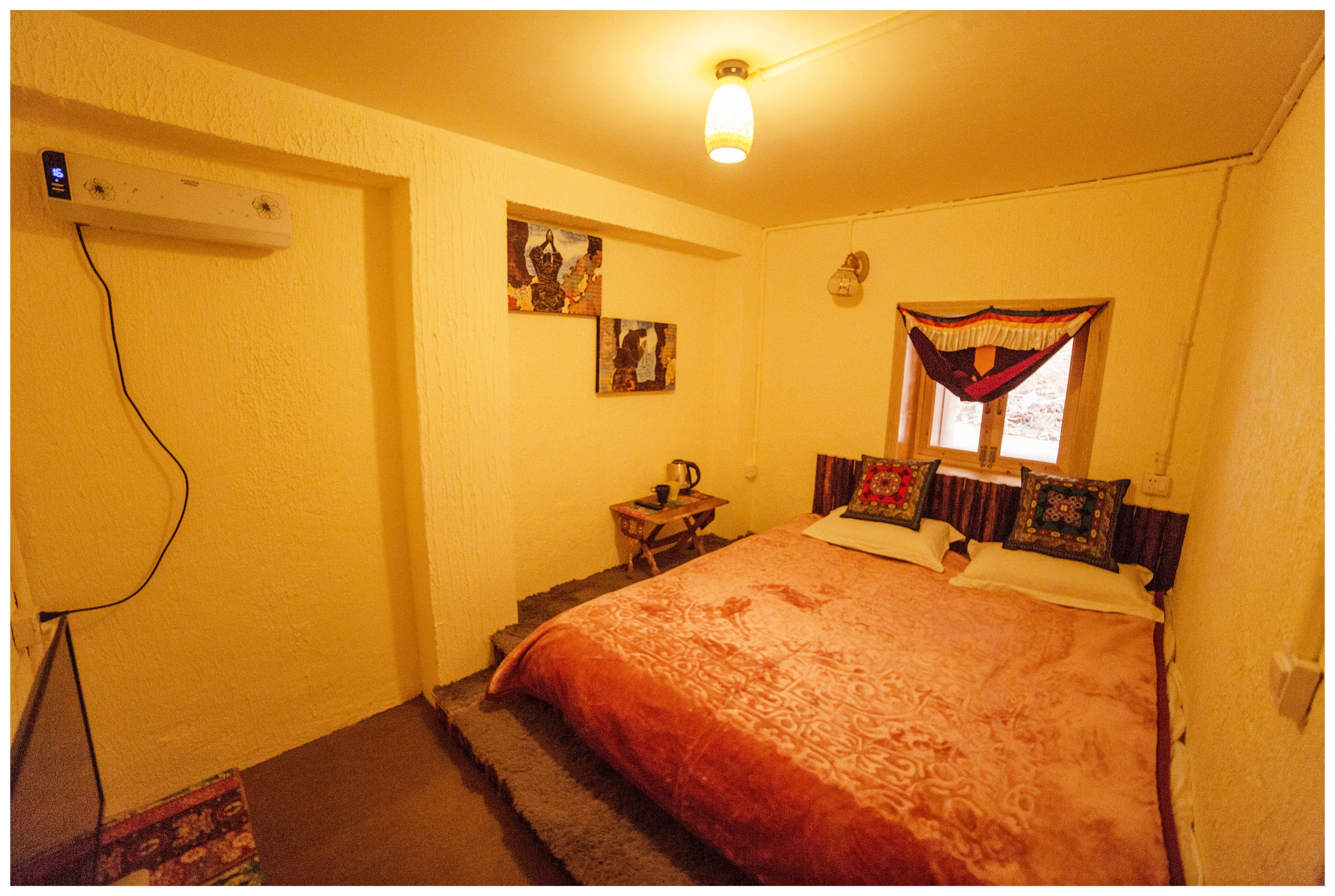 Un dormitorio con una cama grande, una mesita de noche, cortinas en la ventana y una lámpara fijada a la pared.