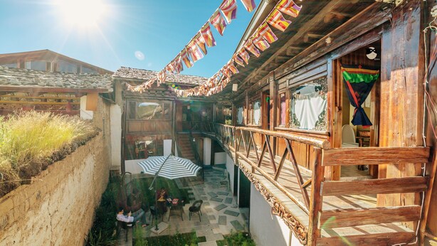 A traditional wooden building with a stone courtyard, a staircase, and a view of the surrounding area. - Yi's Hostel (Deqin)