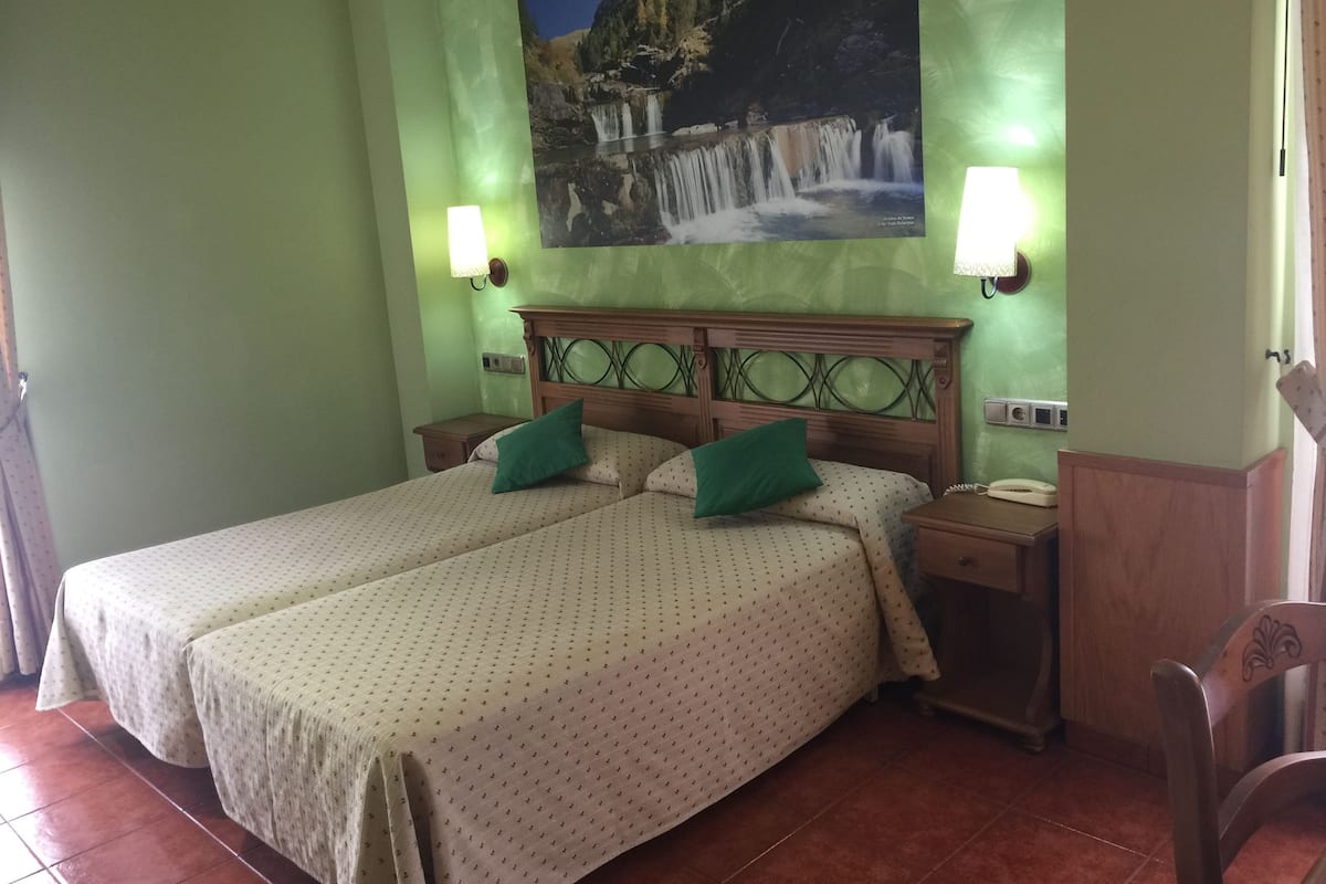 Una habitación de hotel con dos camas, cabeceros de madera, mesitas de noche y un cuadro de una cascada en la pared.