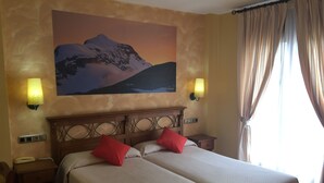 Un letto matrimoniale con due cuscini rossi, un comodino con una lampada, un telefono e un quadro raffigurante una montagna al muro.