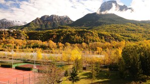 Un campo da tennis circondato da alberi dai colori autunnali e montagne sullo sfondo.