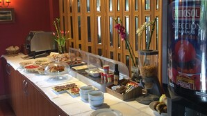 Un buffet allestito con diversi cibi, un dispenser per bevande e un vaso decorativo con fiori.