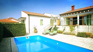 Une piscine avec des chaises longues, un escalier et un bâtiment blanc doté d’un toit en tuiles.