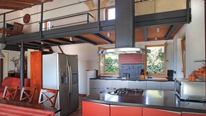 Une cuisine dotée d’un îlot central, un coin repas avec une table et des chaises, et un espace détente aménagé en mezzanine.