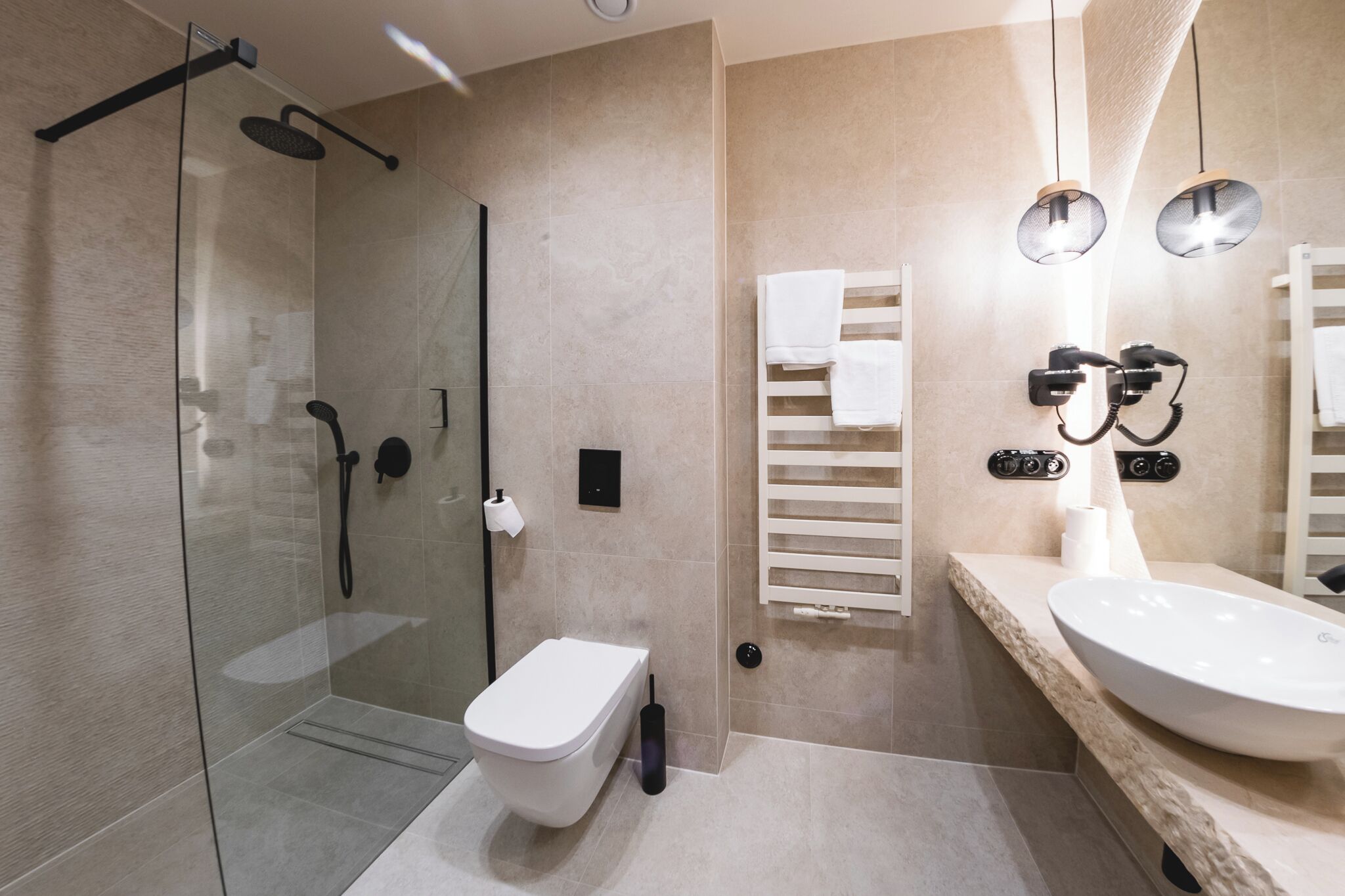 Un baño moderno con ducha de vidrio, inodoro blanco y un lavamanos amplio con espejo.