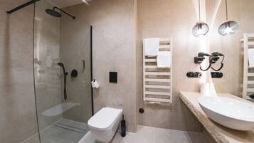 Un baño moderno con ducha de vidrio, inodoro blanco y un lavamanos amplio con espejo.