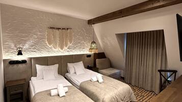 A hotel room with two beds, a desk, a chair, a large window with curtains, and a textured wall.