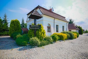 A white building with a sign reading "HOTEL RESTAURACJA" and a cobblestone path leading to it. - Dwór Bogucin Hotel & Restauracja (Garbow)