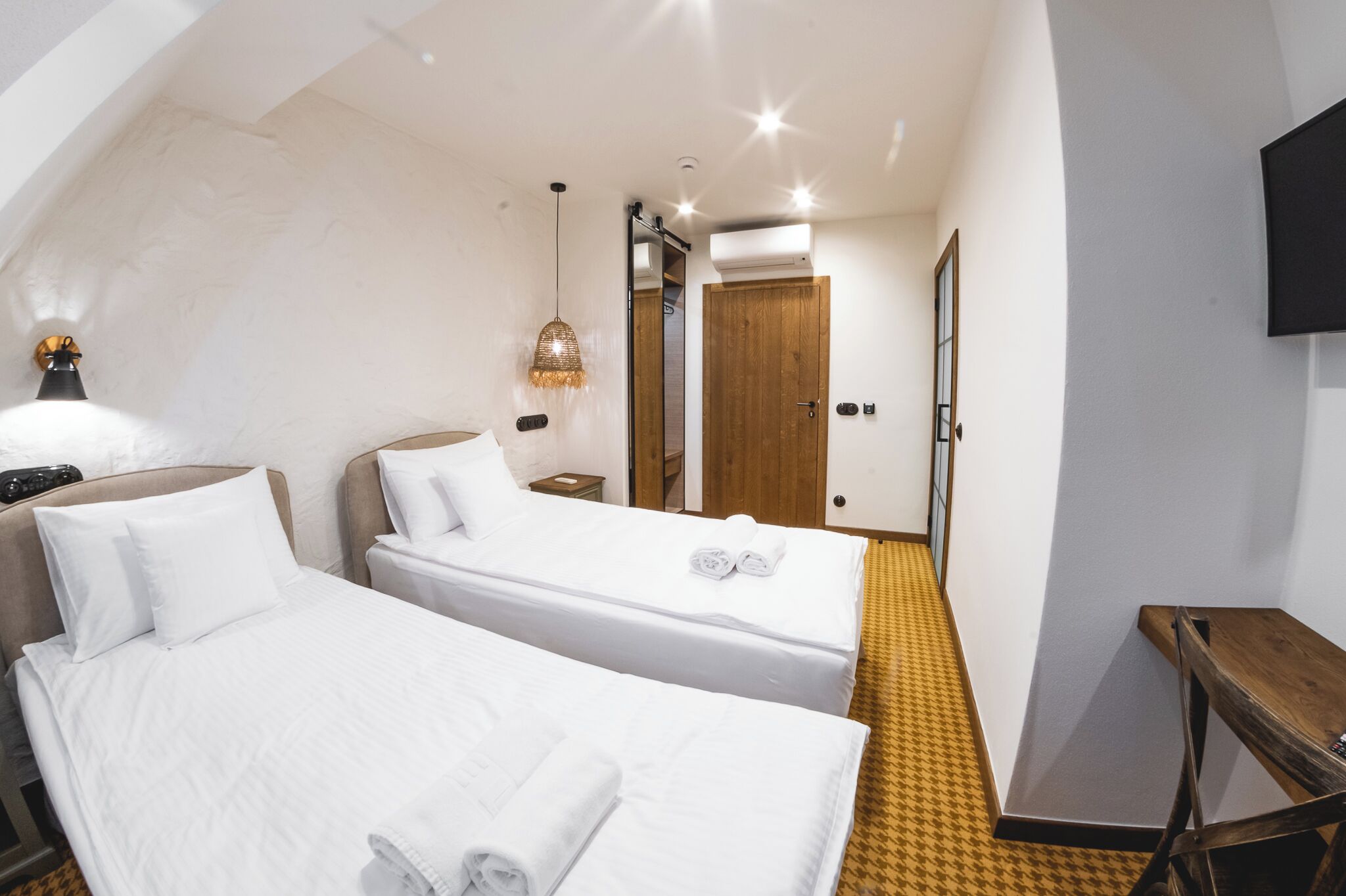 A hotel room with two beds, a wooden bench, a TV, and a mirror.