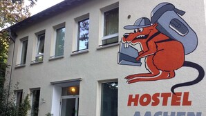 Un edificio con un letrero que dice "HOSTEL AACHEN" y un canguro de caricatura usando un sombrero y llevando una maleta.