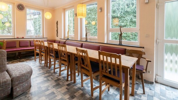 Un comedor con mesas y bancos de madera, ventanas amplias con vistas a la vegetación y lámparas colgantes.