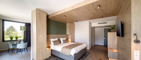 A modern bedroom with a large bed, a desk, and a TV mounted on the wall.