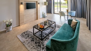 A modern living room with a teal sofa, a glass coffee table, and a flat-screen TV mounted on a wooden wall. - Hotel 46 (Wintelre)