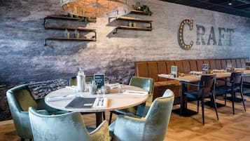 A restaurant with round tables, cushioned chairs, and a wall with the word "CRAFT" illuminated.