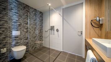 Un baño moderno con cabina de ducha de vidrio, inodoro blanco y tocador de madera con lavamanos.