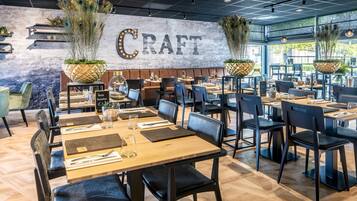 A restaurant interior with a 'CRAFT' sign, wooden tables, black chairs, and potted plants.