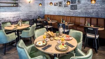 Ein Restaurant mit runden Tischen, grünen Sitzmöbeln und einer rustikalen Wand mit hängenden Lampen.