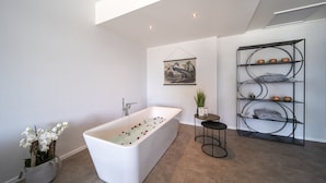 A modern bathroom with a freestanding bathtub, a wall-mounted shelf with decorative items, and a potted plant. - Hotel 46 (Wintelre)