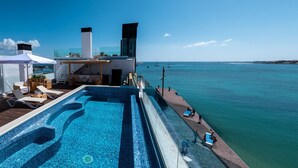A rooftop infinity pool with a clear view of the ocean, a lounge area with sunbeds, and a modern building with a glass facade. - Hotel Boutique La Marquesina - Adults Only (La Oliva)
