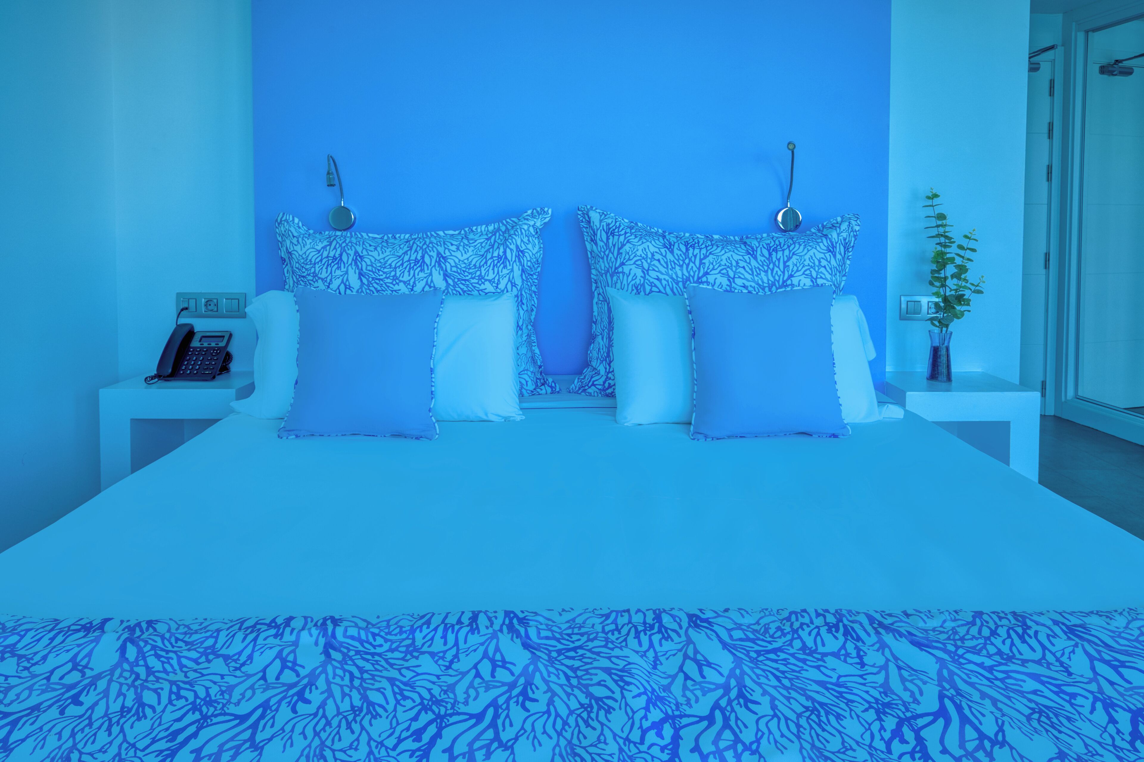 A bedroom with a bed, two bedside tables, a nightstand, a telephone, and a plant.