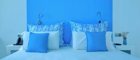 Una habitación de hotel moderna con una cama grande, dos lámparas de noche, una mesita de noche con un teléfono y un jarrón con flores secas.