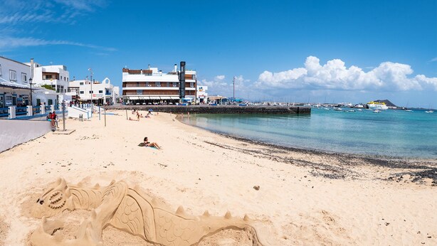 A beach with a sandy shore, a pier, and buildings in the background. - Hotel Boutique La Marquesina - Adults Only (La Oliva)
