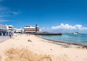 Ein Strand mit sandigem Ufer, einem Steg und Gebäuden im Hintergrund.
