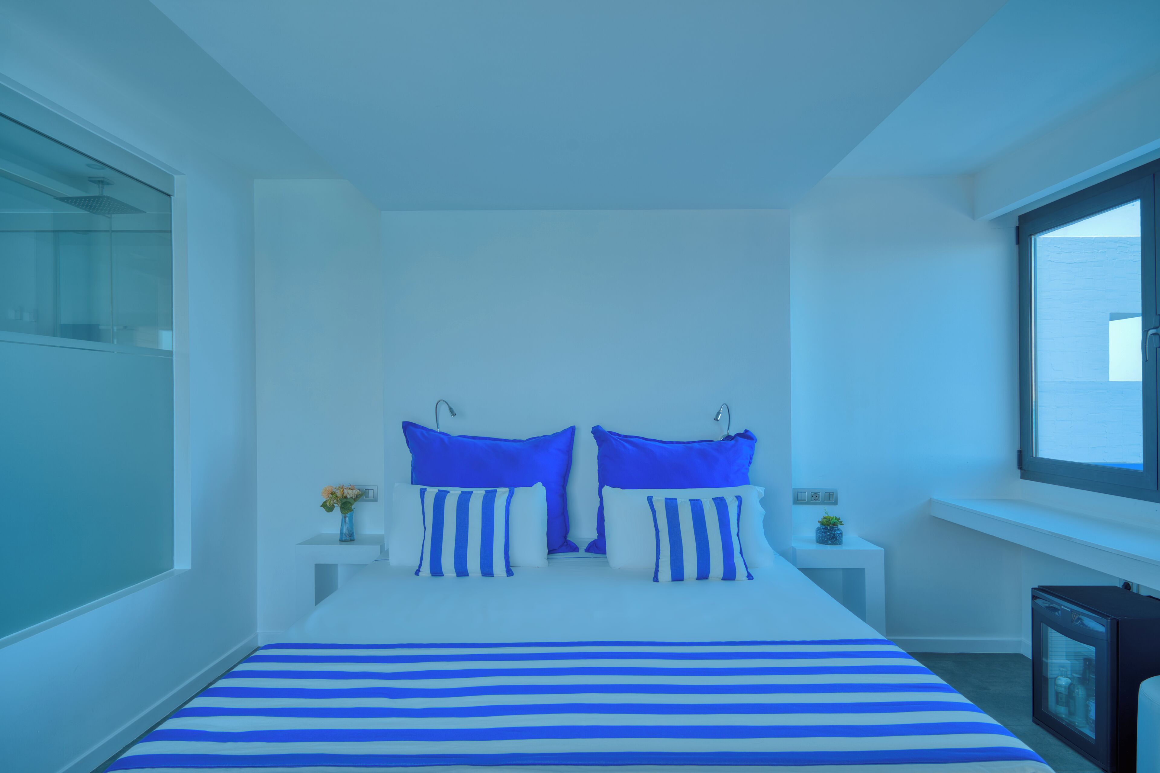 Ein Schlafzimmer mit einem Bett, zwei Nachttischen, einem Fenster und einem kleinen Tisch mit einer Vase.