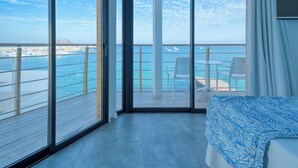 A balcony with a view of the sea and boats, a bed with a patterned bedspread, and a TV on the wall. - Hotel Boutique La Marquesina - Adults Only (La Oliva)