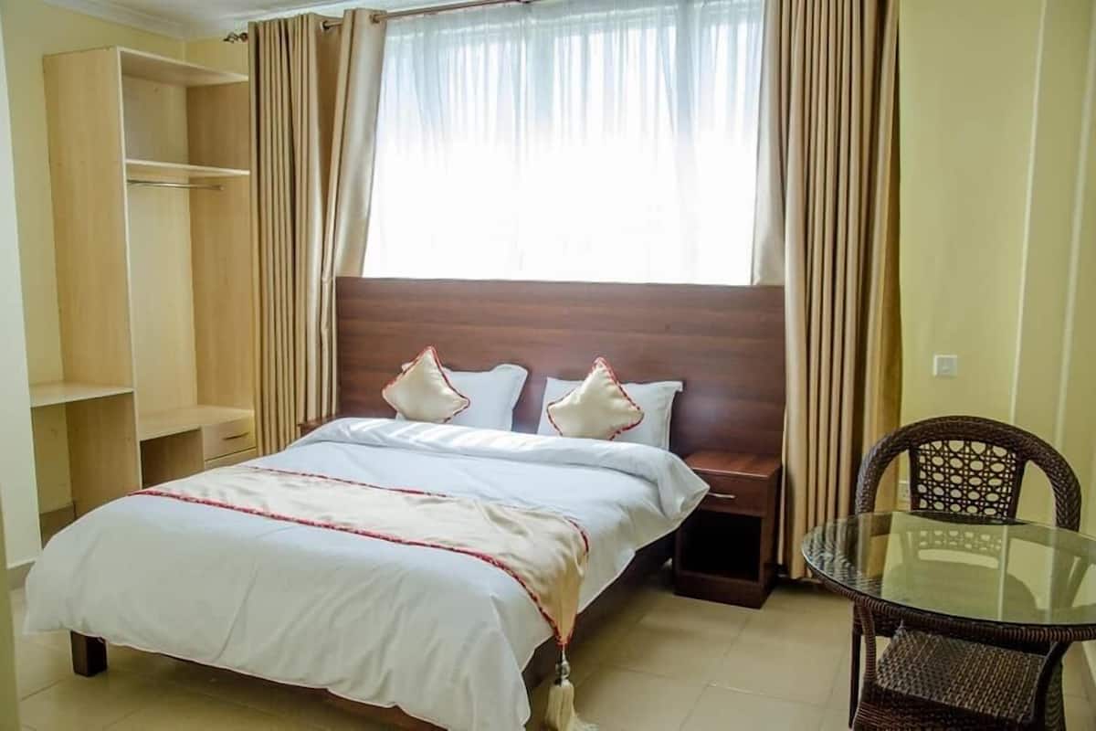 Quarto com cama, mesa de cabeceira, mesa de vidro e uma cadeira.