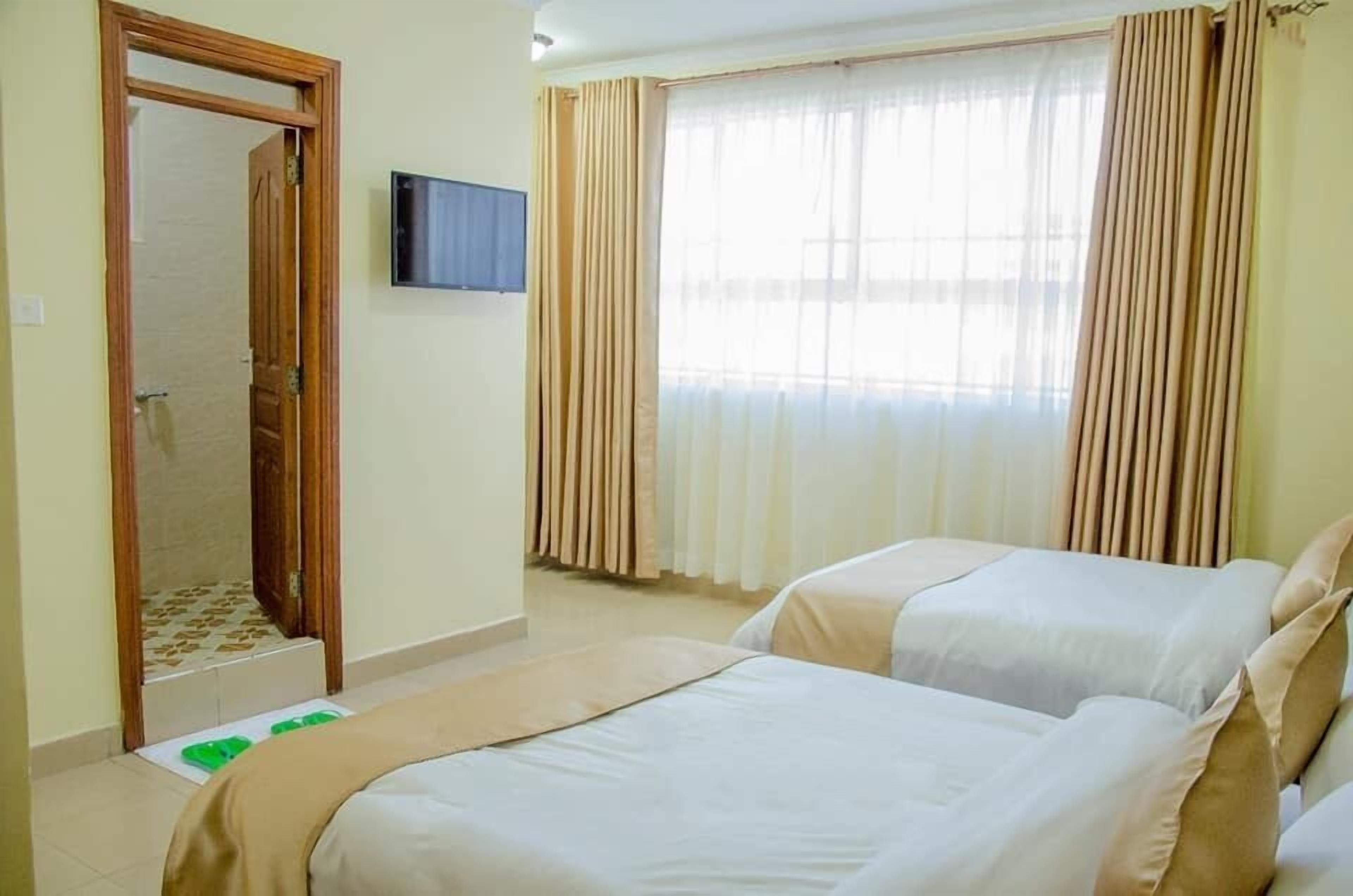 A hotel room with two beds, a television on the wall, and a window with curtains.