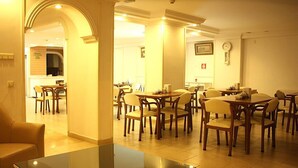 Une salle à manger d’hôtel avec plusieurs tables et chaises, un comptoir de réception et une horloge au mur.