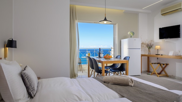 Ein Hotelzimmer mit Bett, Schreibtisch mit Stuhl, Esstisch mit Stühlen, Fernseher und Meerblick.