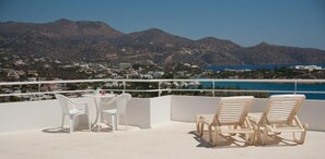 A terrace with white chairs and a table, overlooking a coastal town and mountains. - Bellevue Suites (Agios Nikolaos)