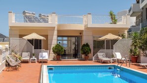 Ein Poolbereich mit Liegestühlen und Sonnenschirmen, ein klarer Himmel und ein Gebäude mit einem Balkon.
