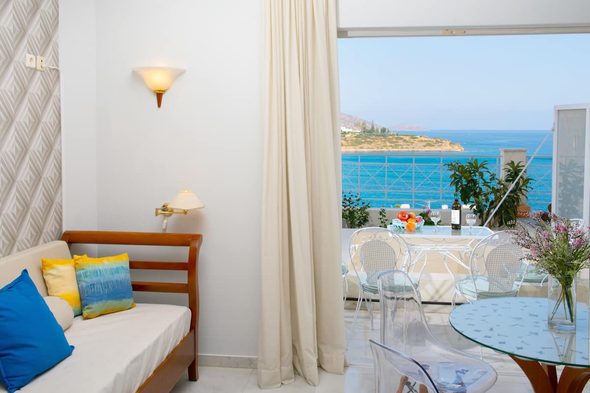 Ein Balkon mit Meerblick, eine Essecke mit Stühlen und Tisch sowie ein Bett mit Kissen.