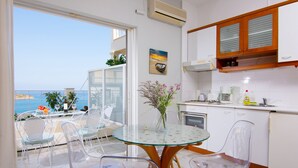 Eine moderne Küche mit einem Glastisch und Stühlen, Meerblick und einem kleinen Balkon mit Sitzgelegenheit.