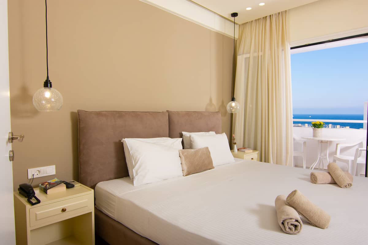Ein Hotelzimmer mit einem großen Bett, einem Nachttisch und Meerblick.