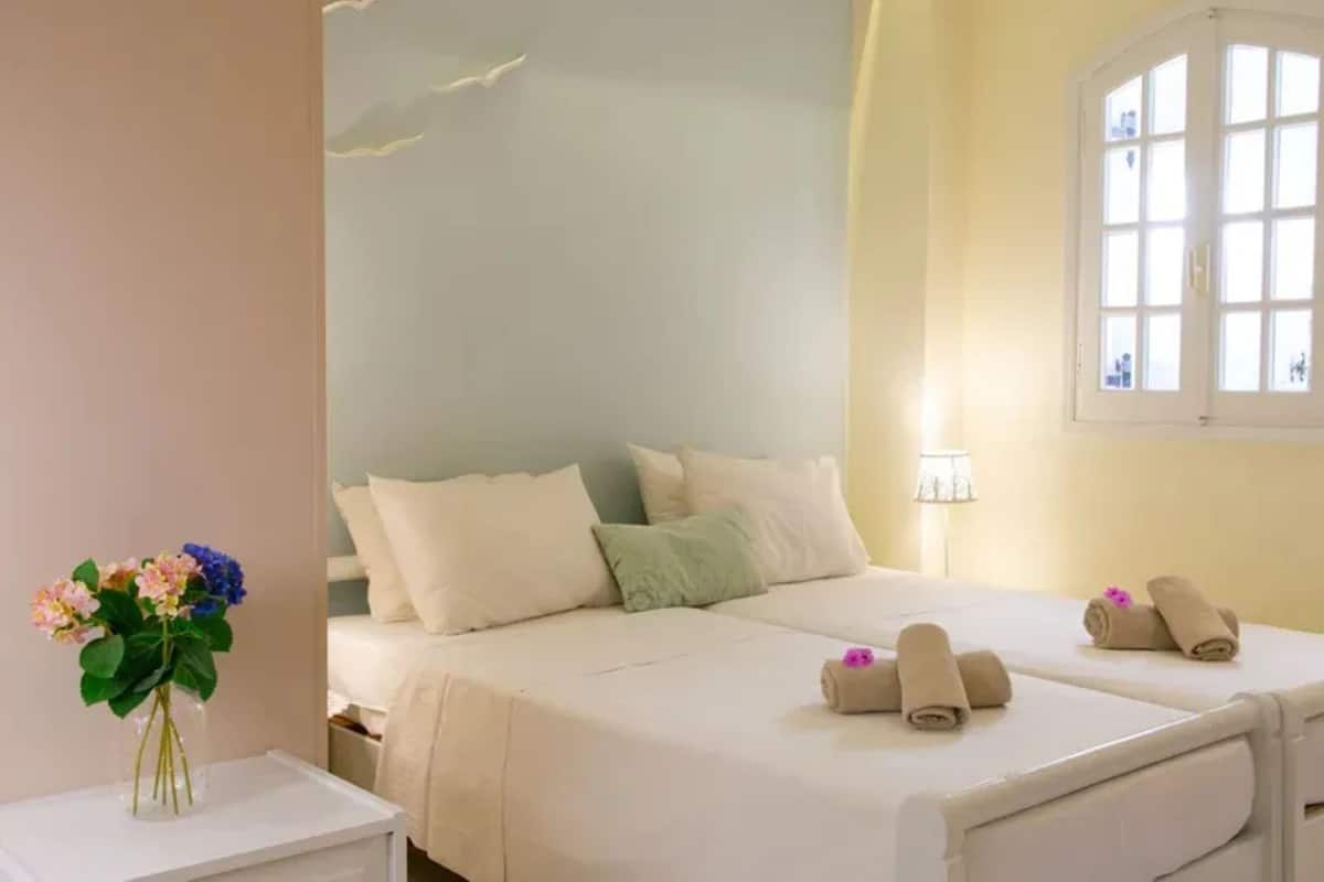Ein Hotelzimmer mit zwei Betten, einem Nachttisch mit Blumenvase und einem Fenster mit Blick.