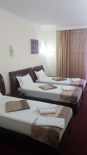 Habitació d'hotel amb tres llits individuals, cadascun amb capçalera de fusta, roba de llit blanca i coixí decoratiu marró.
