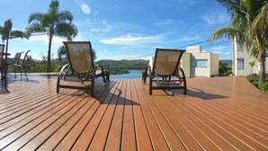 Una terraza de madera con dos sillones de descanso frente a una vista panorámica de un lago y montañas.